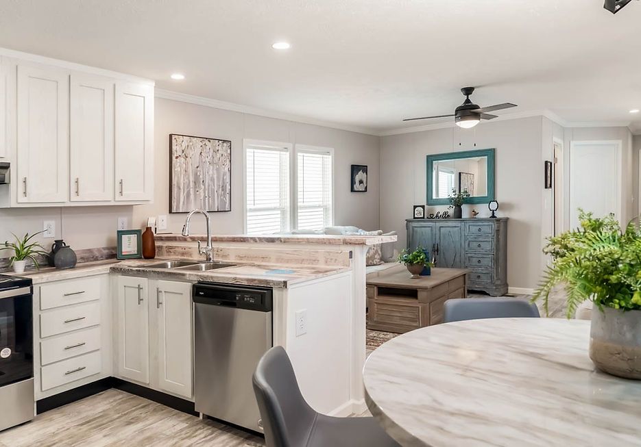 A bright kitchen and living area with white cabinets, stainless steel appliances, and a round dining table.
