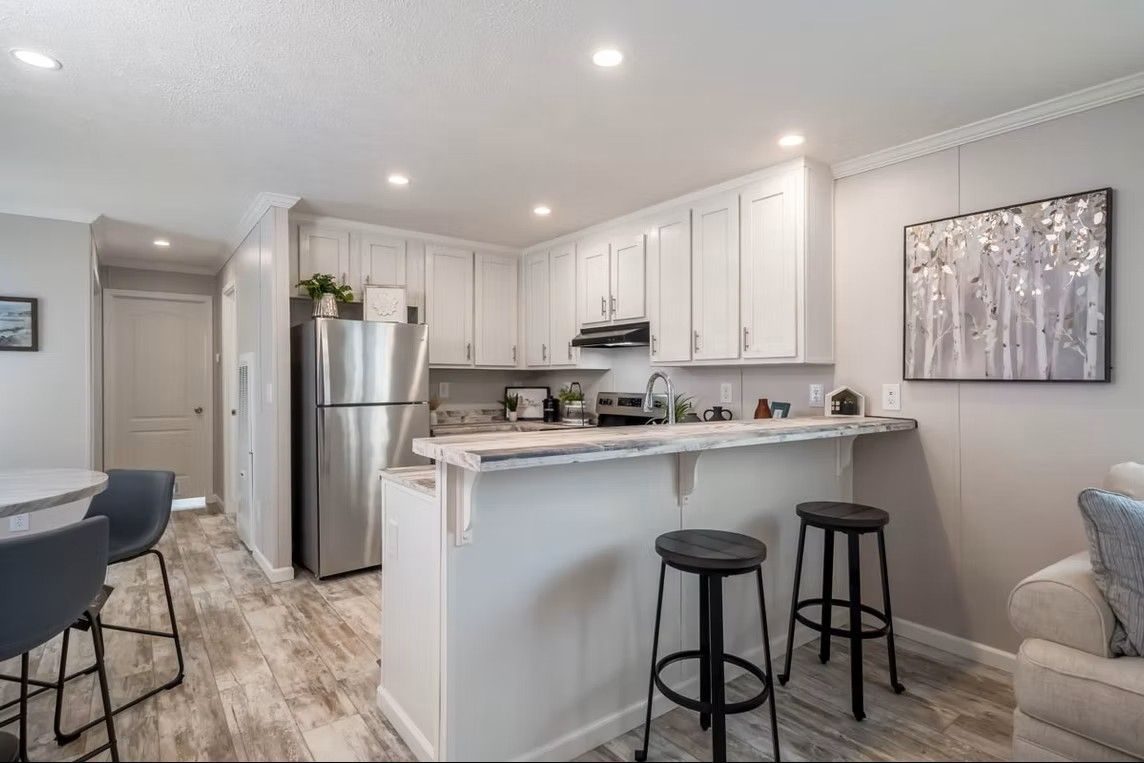 White kitchen with stainless steel appliances, breakfast bar with stools, and light wood flooring.