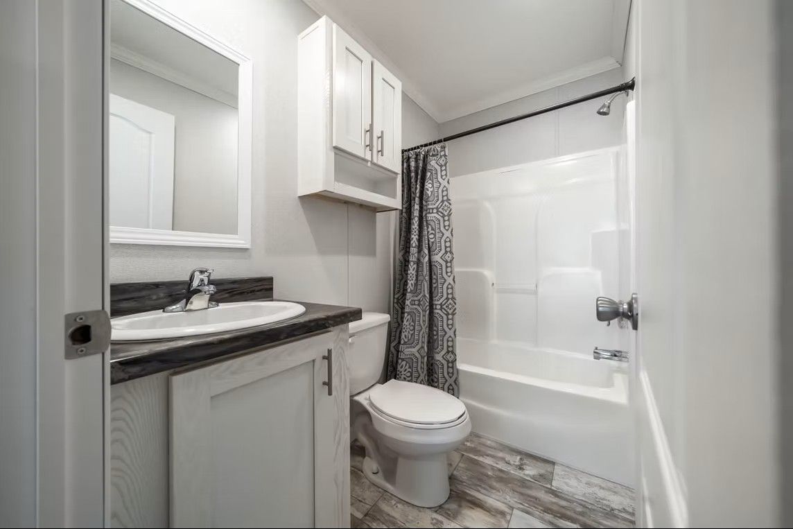 Bathroom with white fixtures, grey countertop, and patterned shower curtain.