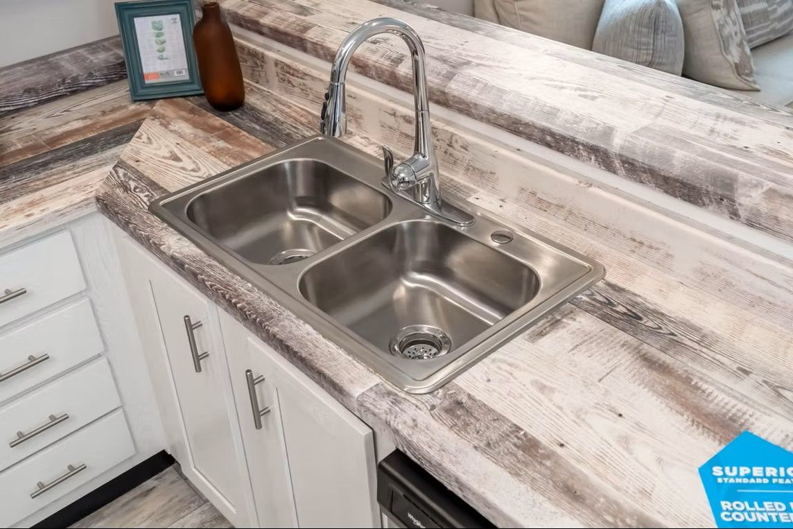 Stainless steel double sink in a kitchen with white cabinets and a weathered countertop.