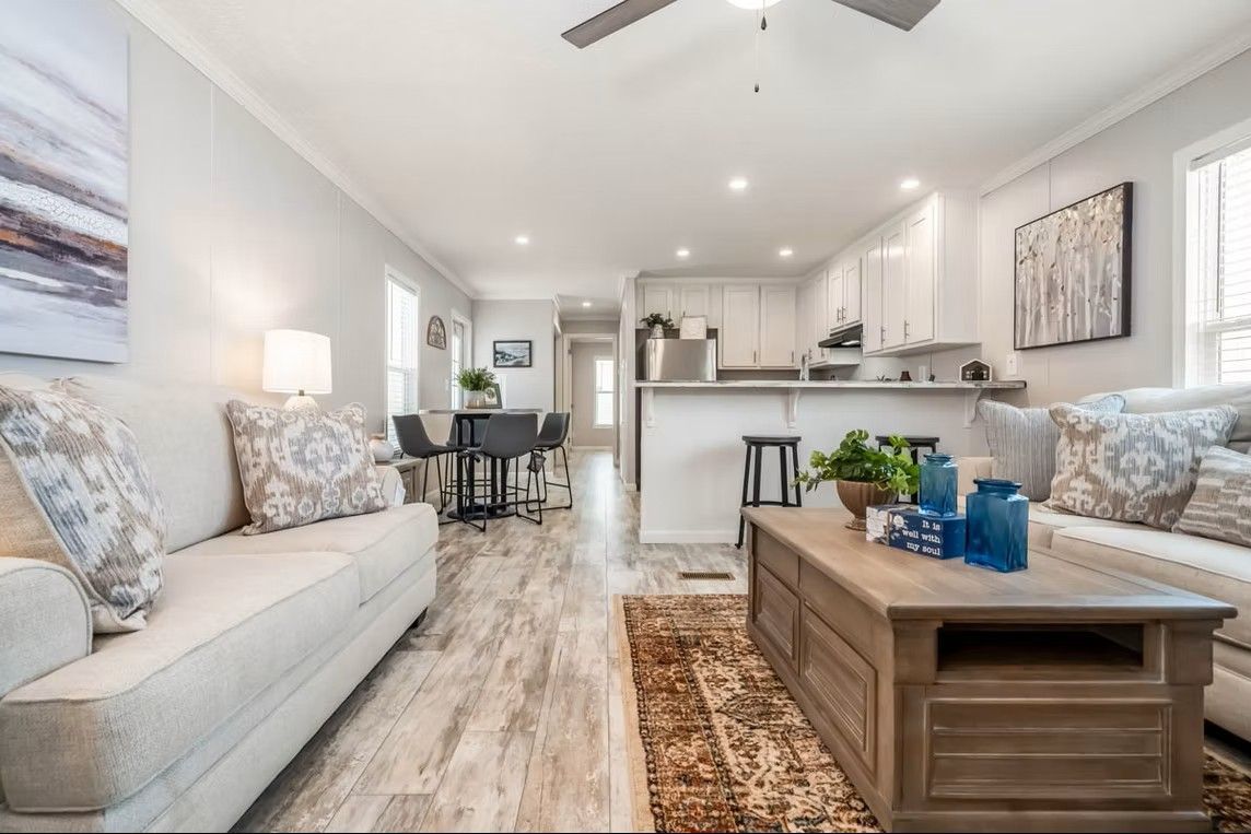 Bright living room with open kitchen, light wood floors, and neutral furniture.