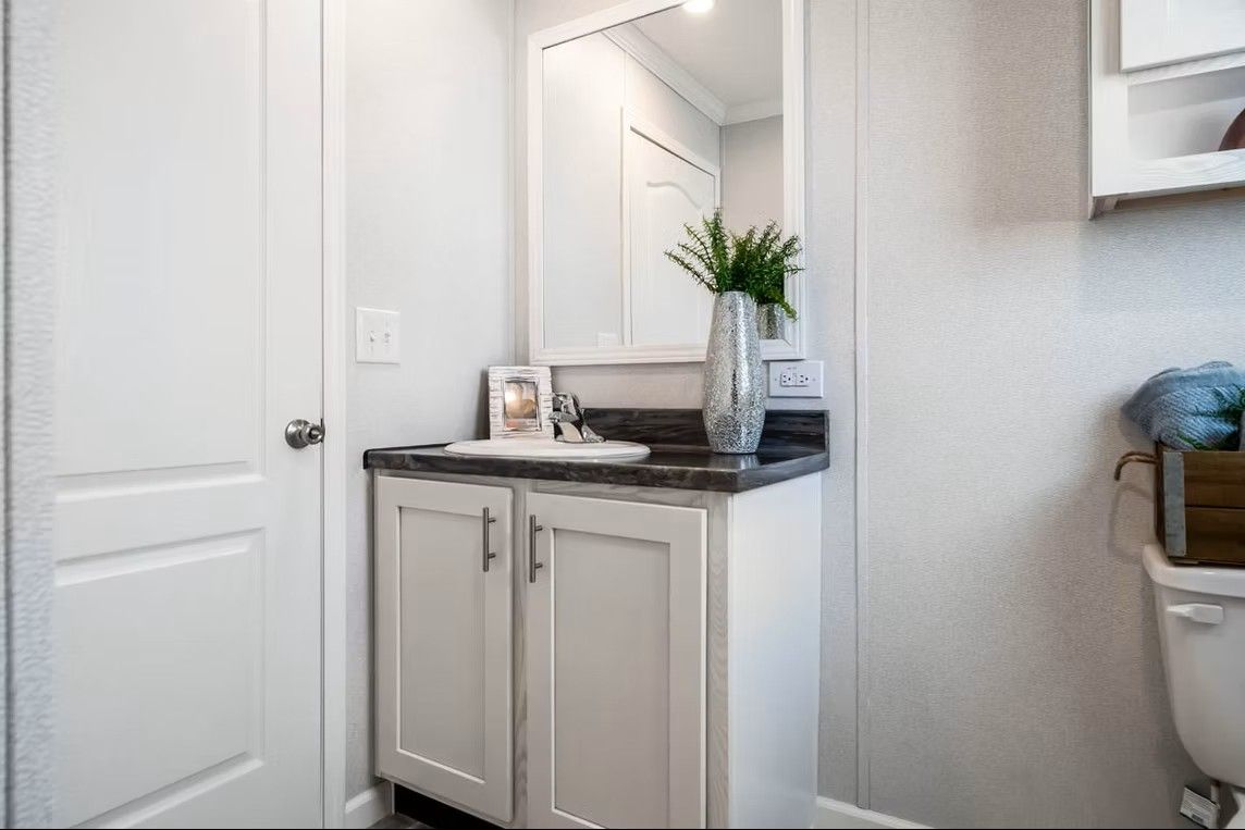 Bathroom with white vanity, gray countertop, mirror, and white door.