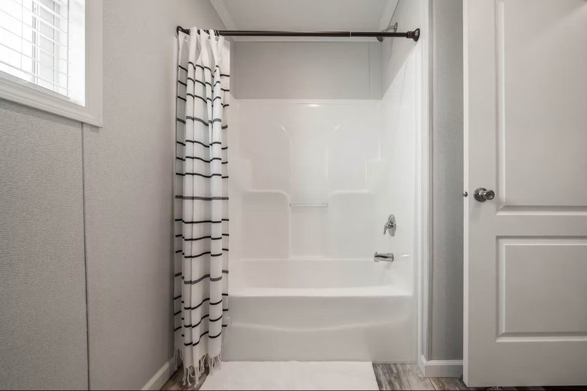 Bathroom with a white tub and shower, gray walls, and a patterned shower curtain.