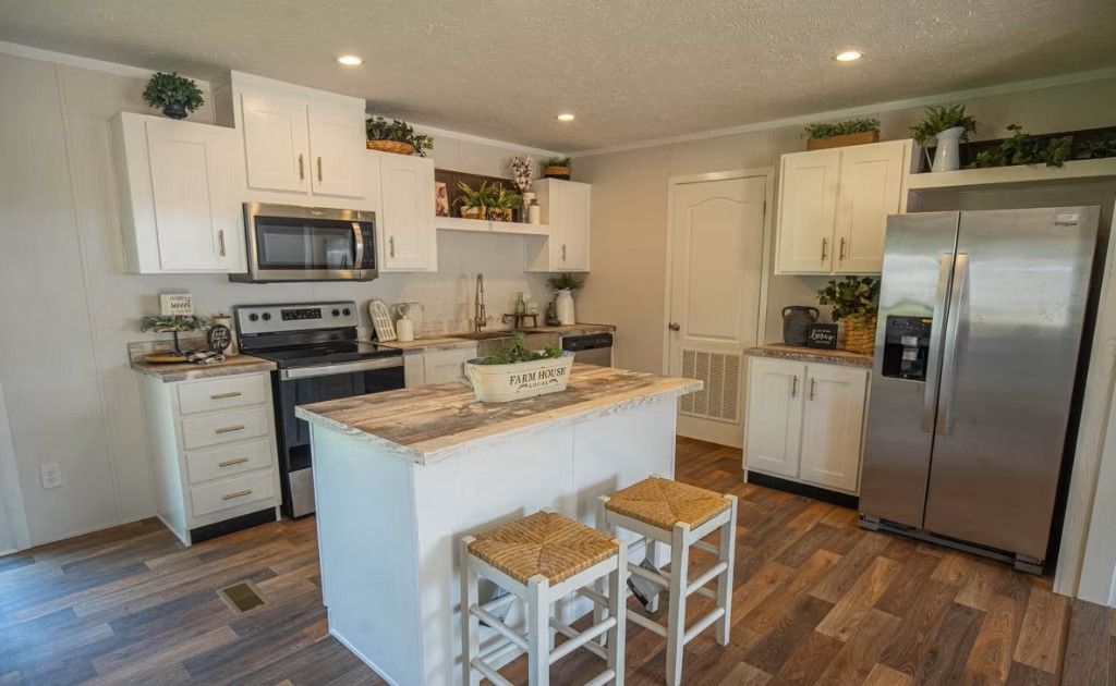 White kitchen with island, stainless steel refrigerator, and wood-look flooring.