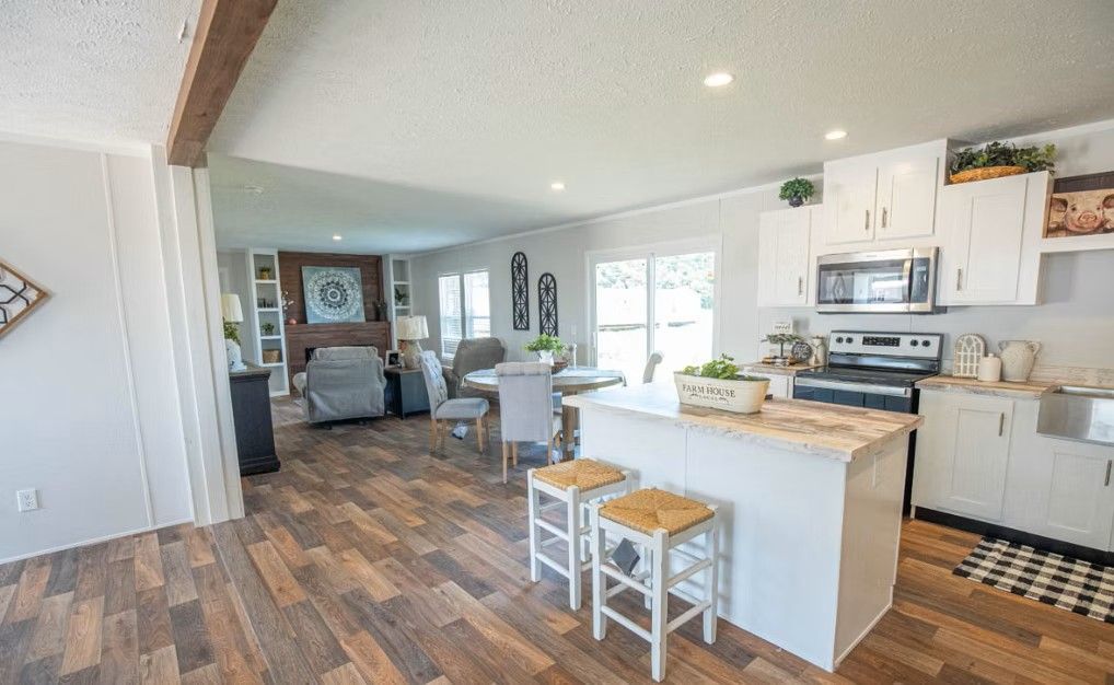 Open-concept kitchen and living room with white cabinets, wood-look flooring, and a stone fireplace.