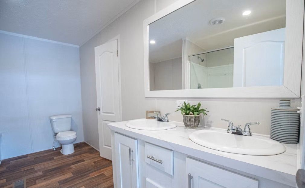 Bathroom with double sink vanity, large mirror, and toilet. White cabinets, wood-look floor, light walls.