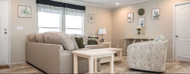 Living room interior with beige furniture, neutral walls, and window with patterned shade.