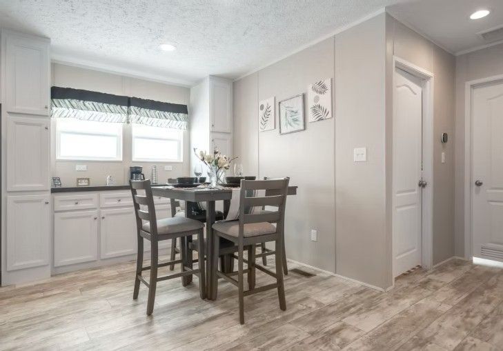 Kitchen and dining area with gray table and chairs, white cabinets, and artwork on a light gray wall.