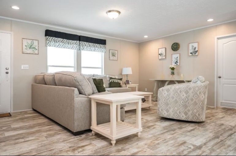 Living room with beige couch, patterned chair, light wood floors, and white walls.