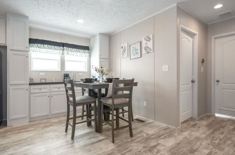 Kitchen and dining area with gray stools and light wood-look flooring. White cabinets and walls.