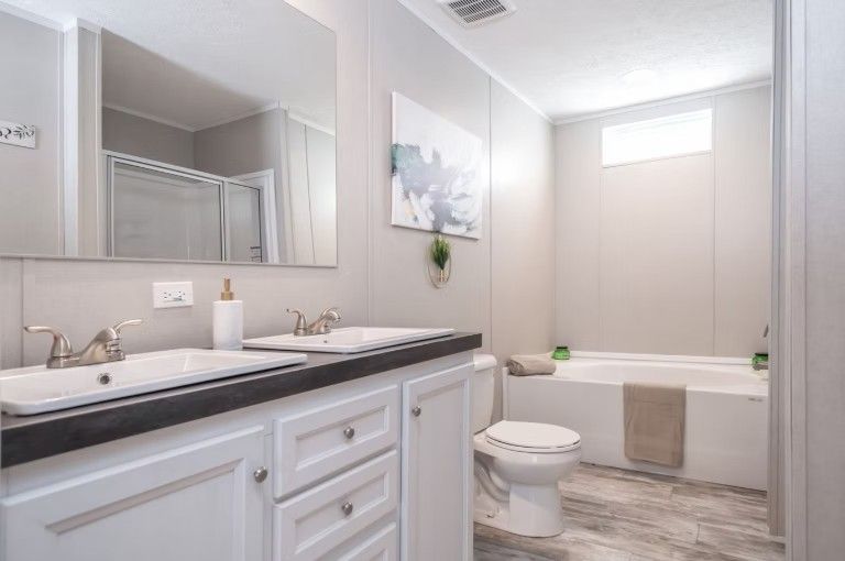 Bathroom with double sinks, white vanity, bathtub, and gray walls.