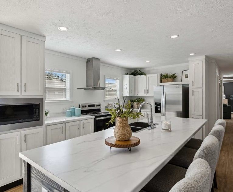 Bright white kitchen with a large island, stainless steel appliances, and wood floors.