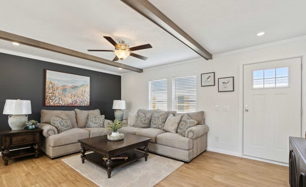Living room with gray sectional, dark accent wall, and wood beams on the ceiling.