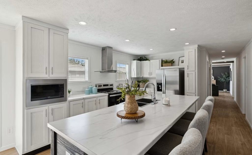 Kitchen with white cabinets, large island, stainless steel appliances, and hallway.