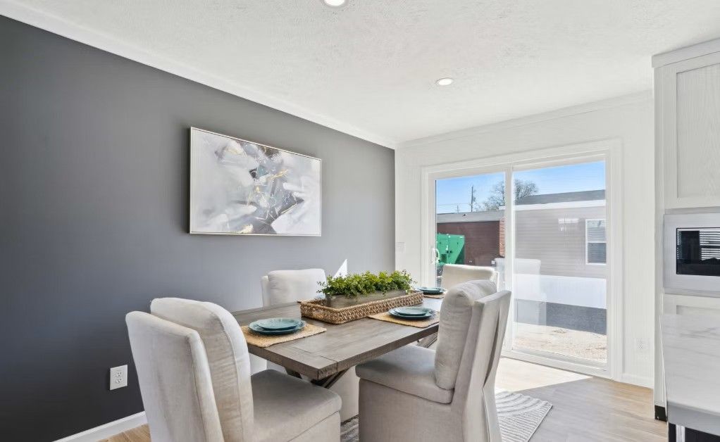 Dining room with gray wall, table, chairs, art, and sliding glass door to a yard.