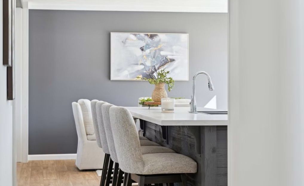 Kitchen island with seating, gray wall, abstract art, vase, candle, and a faucet.
