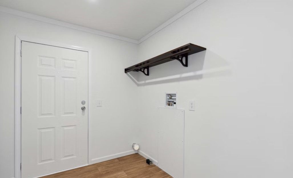 White-walled utility room with a closed white door, a black shelf, and a clothes drying rack.