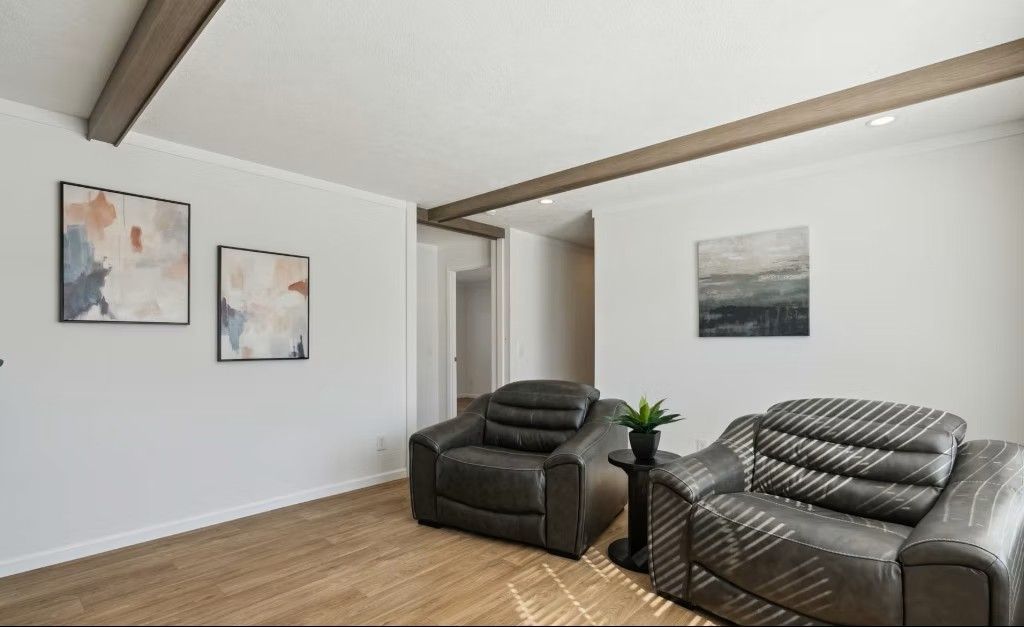 Two gray armchairs in a bright room with light-colored walls, artwork, and exposed wooden beams on the ceiling.
