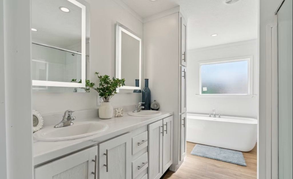 White bathroom with double sinks, mirrors, and a freestanding tub.