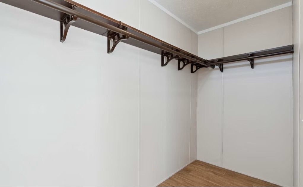Empty walk-in closet with brown shelving and rods, beige walls, and wood-look flooring.