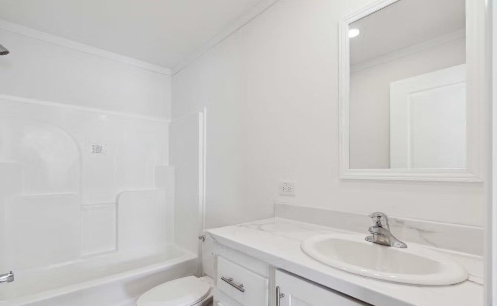 White bathroom with a bathtub, toilet, vanity, and mirror.