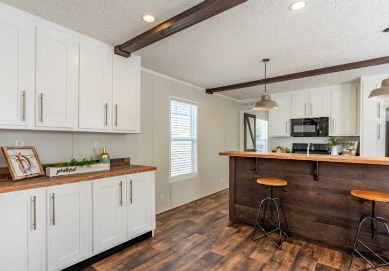 White kitchen with butcher block counters, island, and wooden beams.