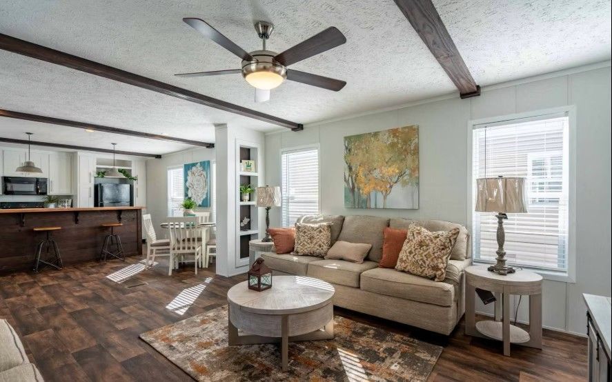 Living room with sofa, coffee table, and dining area in a modern home. Brown wooden beams, hardwood floor.