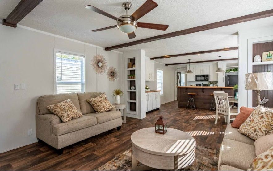 Cozy living room with brown wood floors, couches, and a view of the kitchen with a dark wood island.