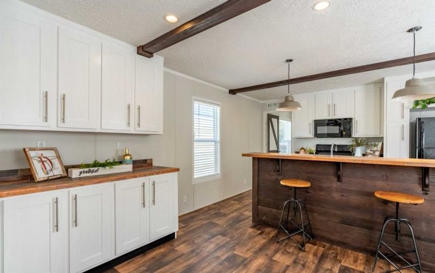 Kitchen with white cabinets, dark wood bar, stools, and brown ceiling beams.