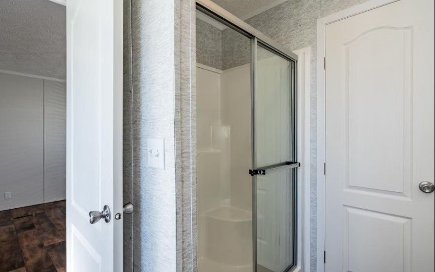Bathroom interior with a glass shower, a closed white door, and a white wall.