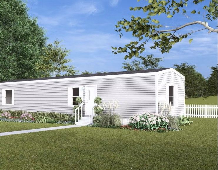 Light gray mobile home with white trim and a white picket fence on a sunny, grassy lawn.