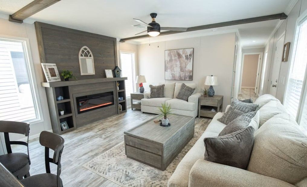 Living room with fireplace, sofas, coffee table, and ceiling fan. Light gray and neutral tones dominate.