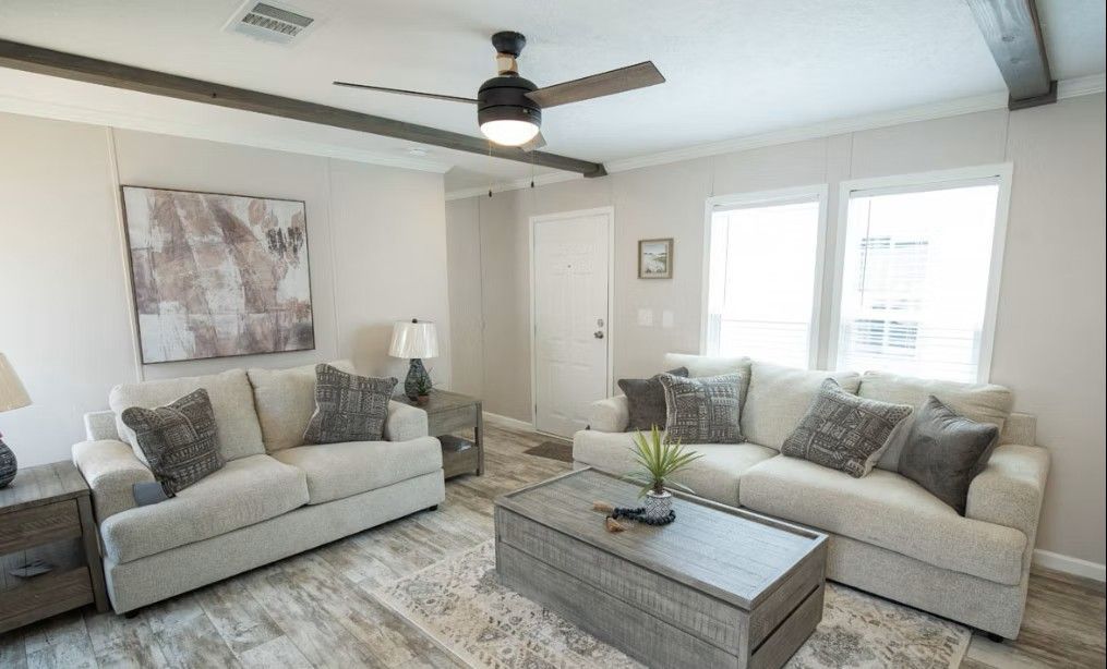 Living room with two cream sofas, gray pillows, wooden coffee table, and large window.
