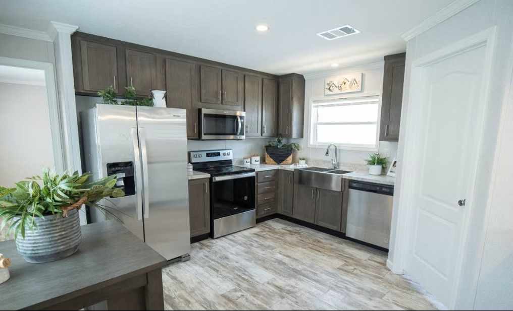 Modern kitchen with stainless steel appliances, dark cabinets, and light wood-look flooring.