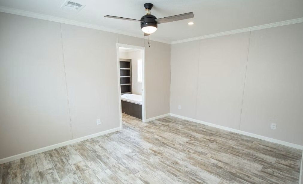 Empty bedroom with light wood-look floor, gray walls, and open doorway to another room.