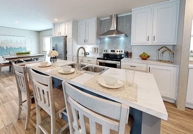 Modern kitchen with island, white cabinets, stainless appliances, and light wood flooring.