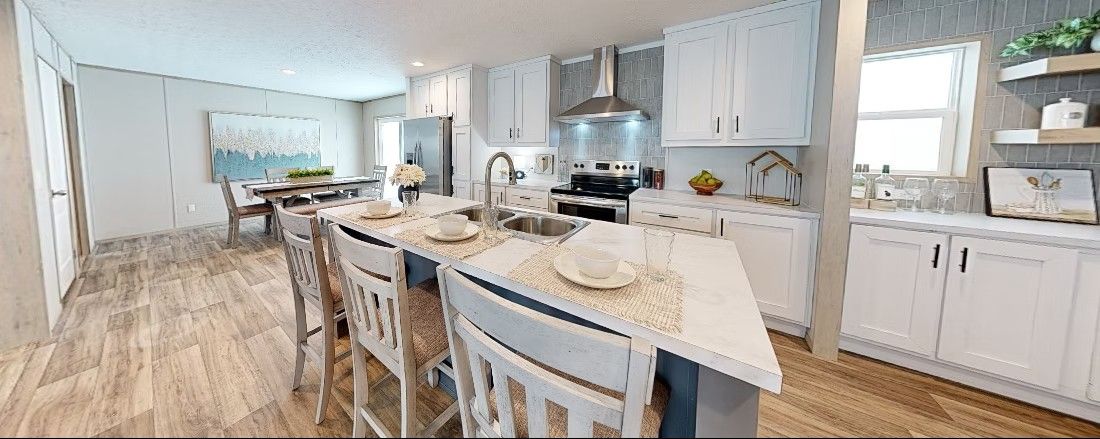 Spacious modern kitchen with island seating, white cabinets, and stainless steel appliances.