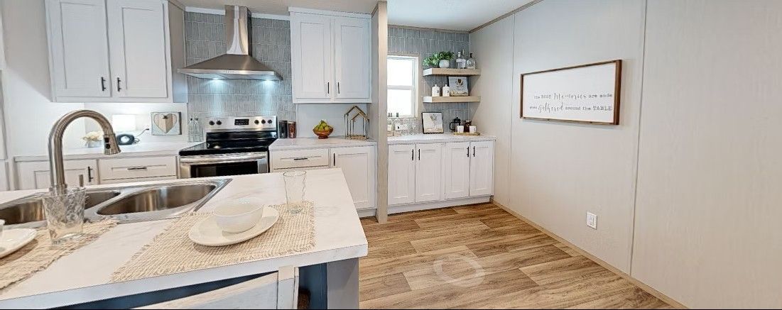 A bright white kitchen with stainless steel appliances and light brown flooring.