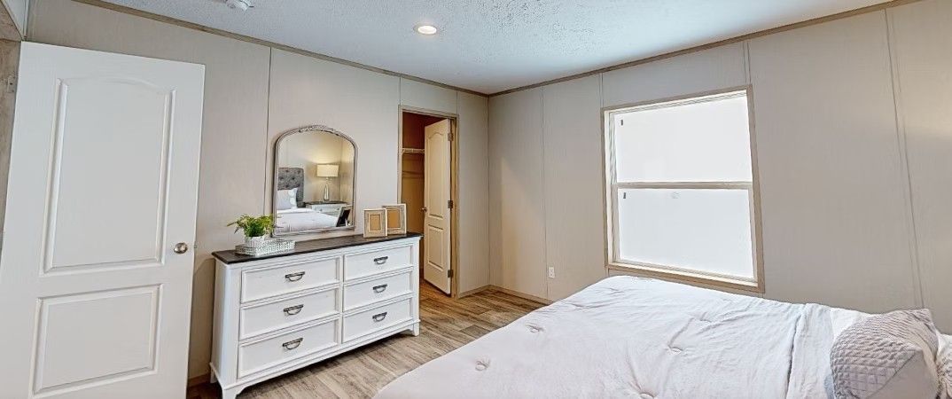 Bedroom interior with white dresser, bed, open closet, and window.