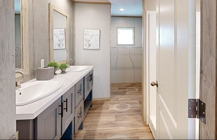 Bathroom with double sink vanity, gray cabinets, light wood floor, and doorway.