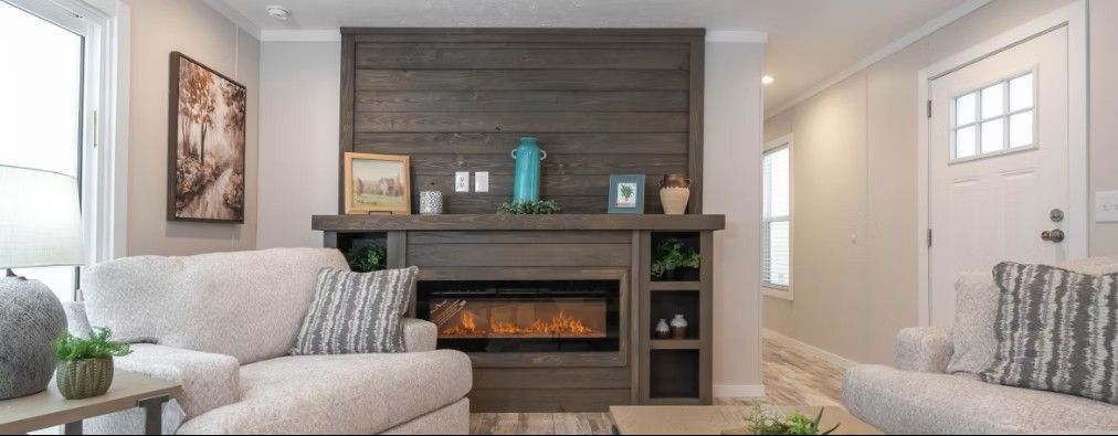 Living room interior featuring a fireplace, two sofas, and decor. The walls are neutral, and the fireplace is wood paneled.