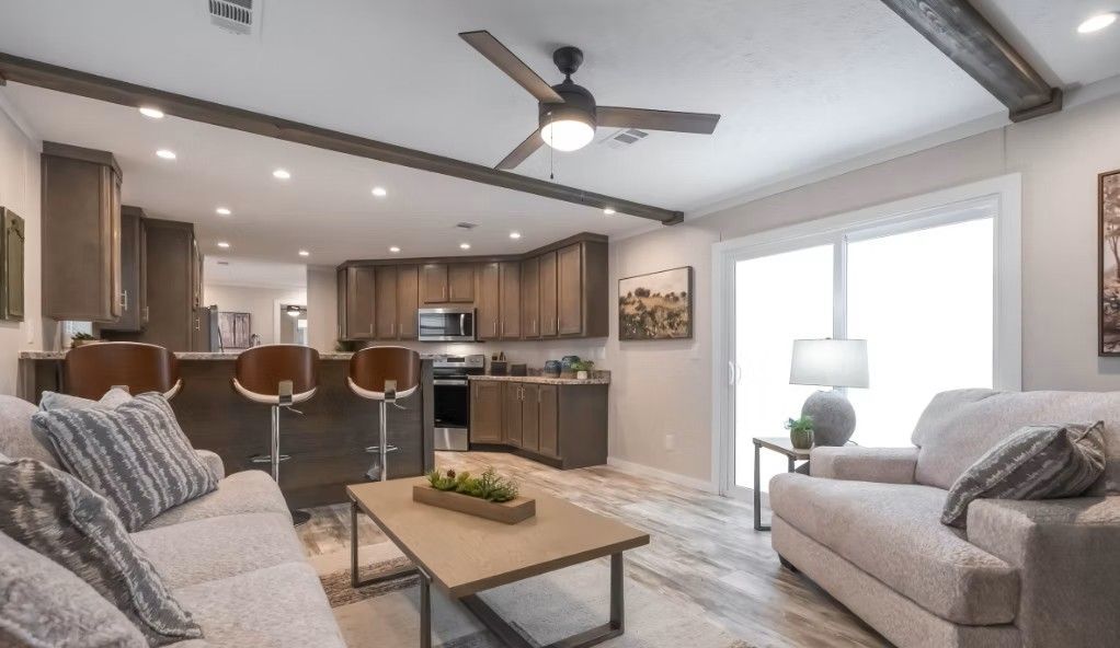 Open-concept living space with kitchen and seating area. Brown cabinets, tan couch, and large windows.