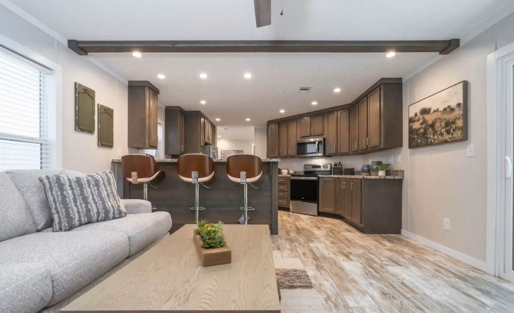 Modern open-concept living area with light wood flooring, kitchen with bar seating, and a sofa.
