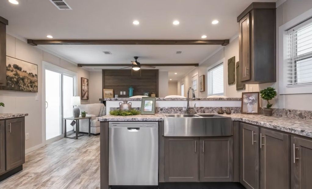 Kitchen with stainless steel dishwasher and sink, brown cabinets, and a living area visible in the background.