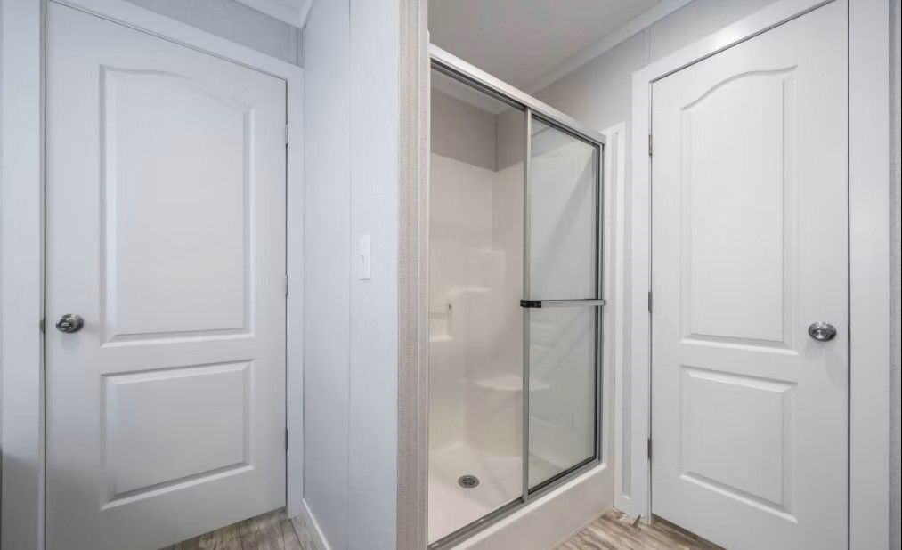 Bathroom with a sliding glass shower door, two white doors, and light gray walls.