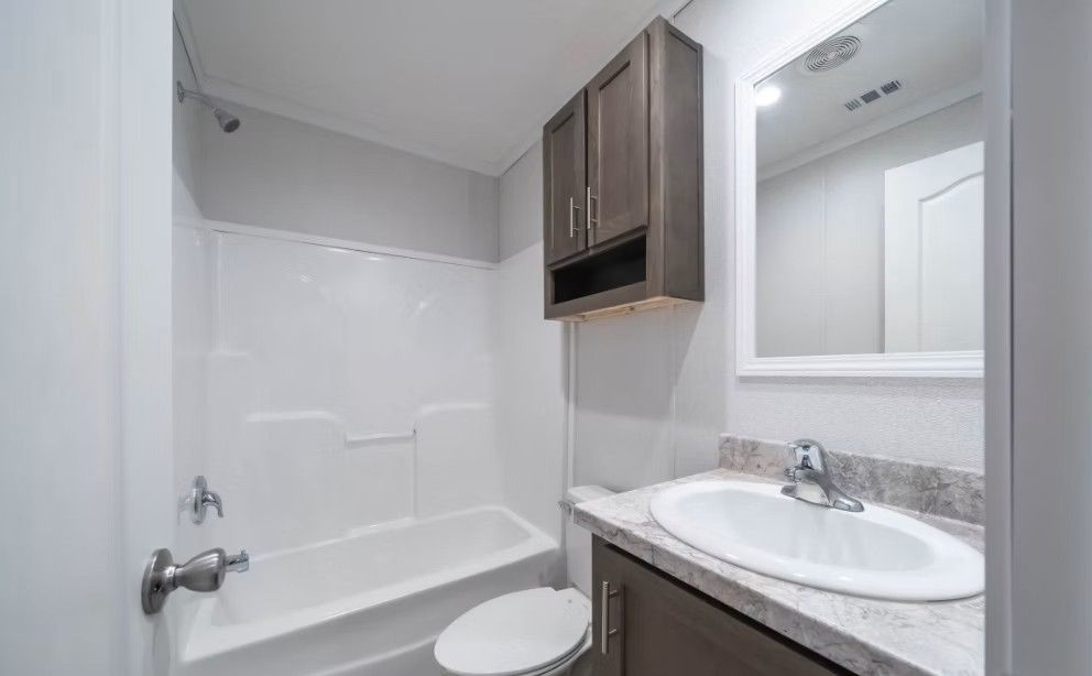 Bathroom with a white tub and toilet, gray vanity, and dark brown cabinet.