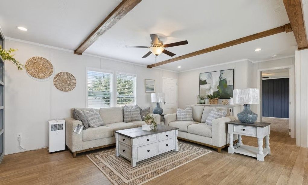Living room with light-colored sofas, wooden beams, a coffee table, and wood flooring.