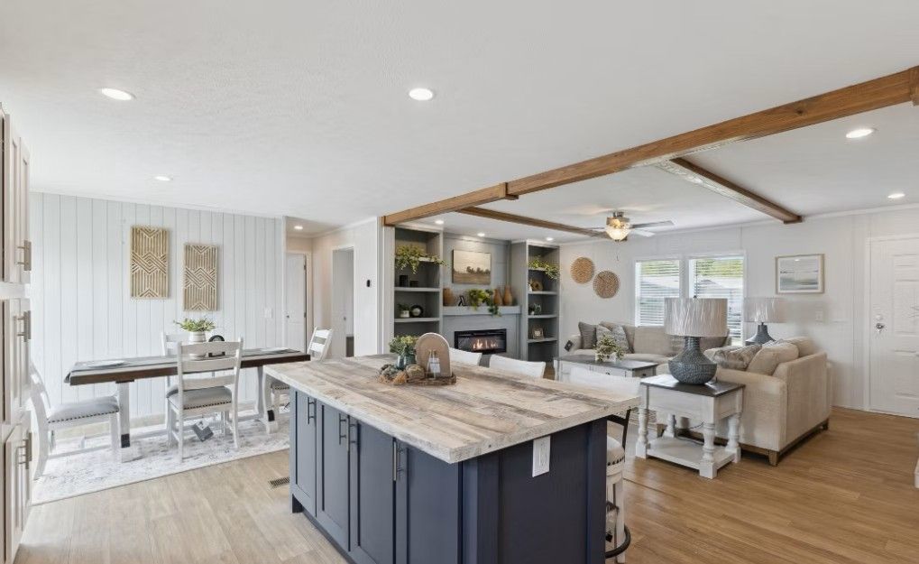 Open-concept living space with blue island, dining area, fireplace, and sofa; light wood floors and white walls.