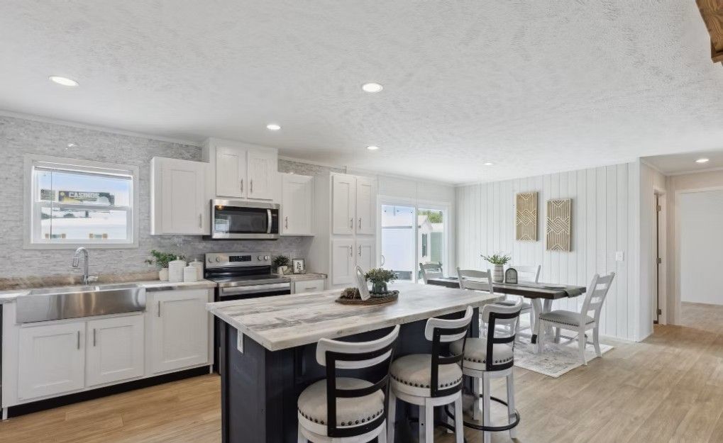 Modern kitchen with white cabinets, dark blue island, stainless steel appliances, and dining area.