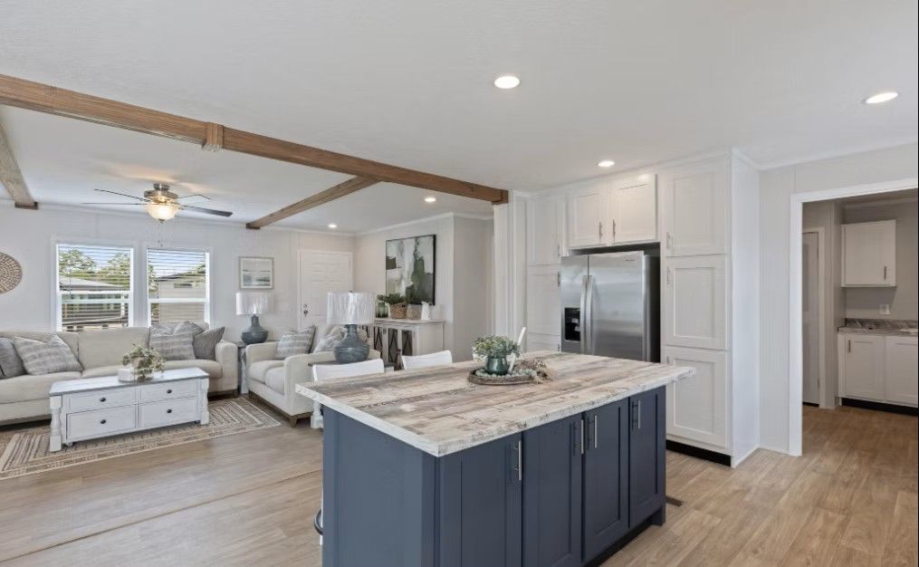 Open-concept kitchen and living room with blue island, white cabinets, and light wood beams.